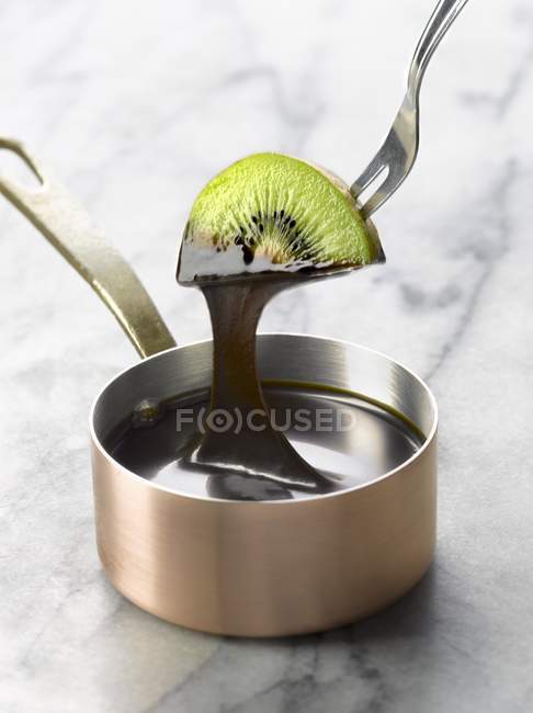 Dipping slice of kiwi into melted chocolate — Stock Photo
