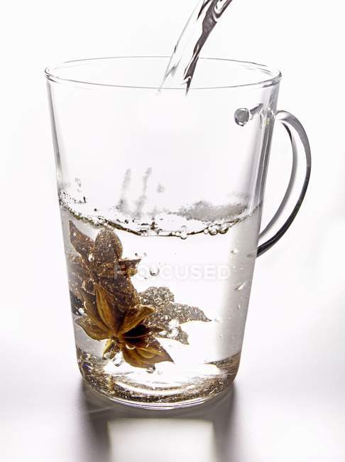 Vista close-up de derramar água em um copo com anis estrela — Fotografia de Stock