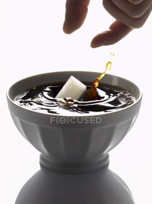Hand Adding lump of sugar to coffee — Stock Photo