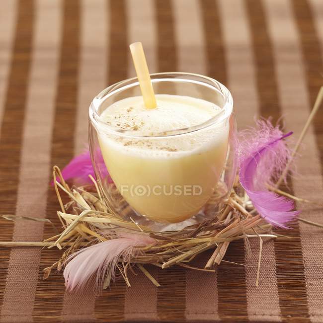 Closeup view of Eggnog in glass with straw in nest — Stock Photo