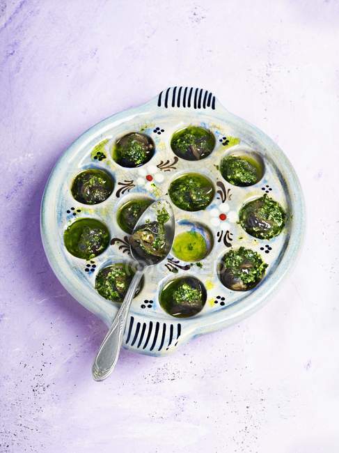 Vue surélevée des escargots cuits verts dans un plat avec cuillère — Photo de stock