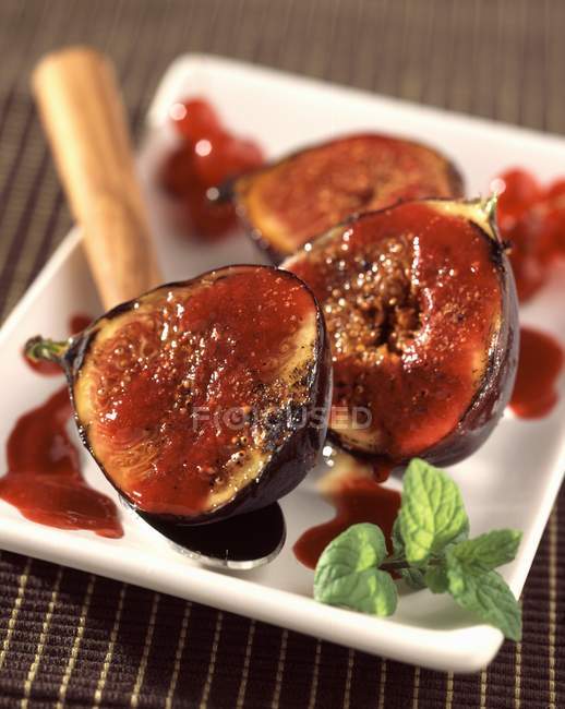 Closeup view of figs halves with sauce and leaves on plate — Stock Photo