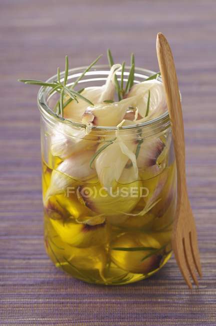 Preserved garlic in olive oil and rosemary in glass with spoon — Stock Photo