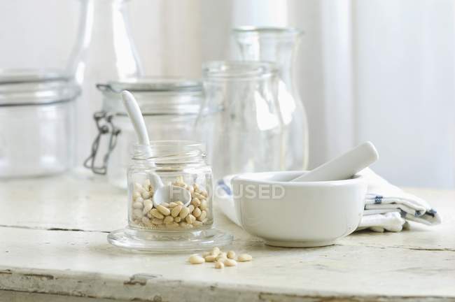 Pine nuts in a glass and mortar on a rustic kitchen table — Stock Photo