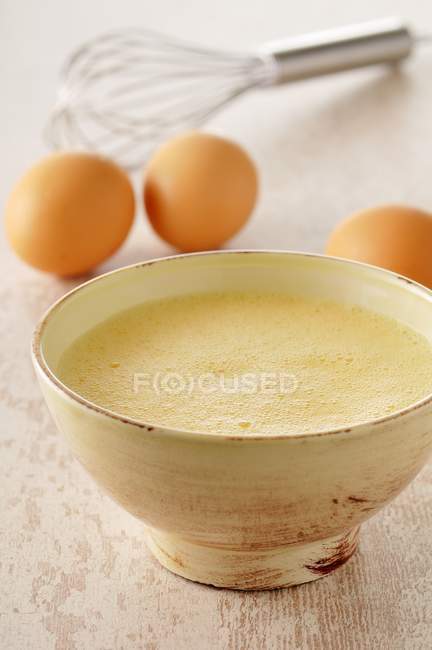 Closeup view of beaten eggs in a bowl and whole eggs nearby — Stock Photo