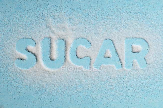 A palavra Açúcar escrito com açúcar na superfície azul — Fotografia de Stock