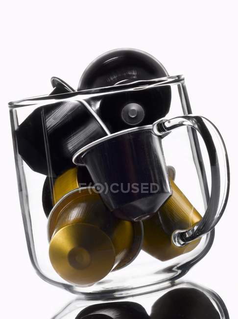 Vue rapprochée des capsules de café pour machine à café Espresso en tasse en verre sur fond blanc — Photo de stock