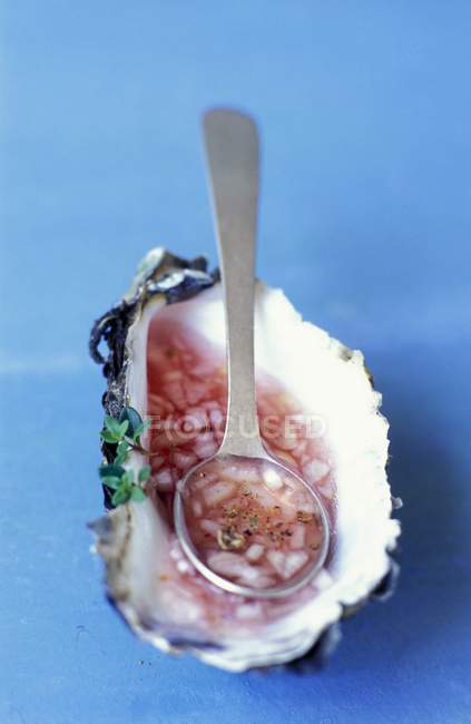 Shallot vinaigrette in an oyster shell and spoon over blue surface — Stock Photo