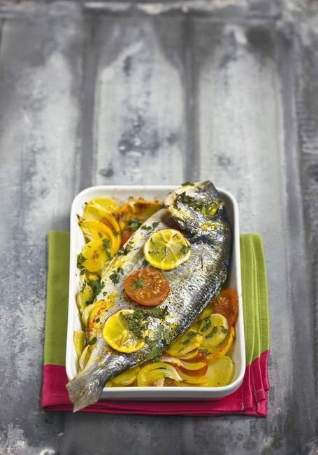 Oven-baked sea bream in white dish over towel — Stock Photo