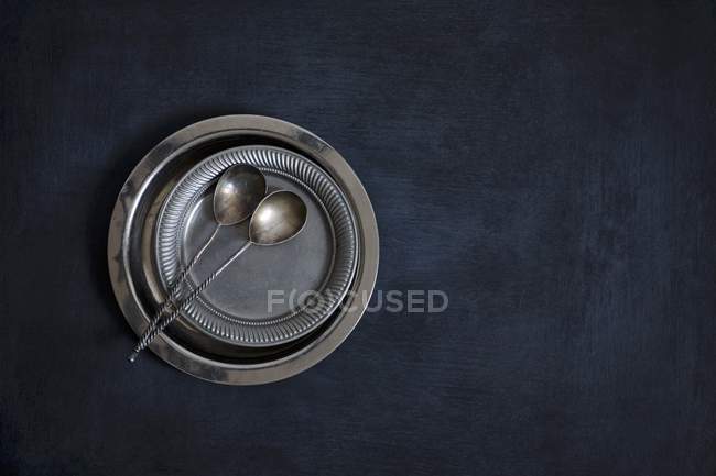 Top view of metal plates and vintage silver spoons on a black background — Stock Photo