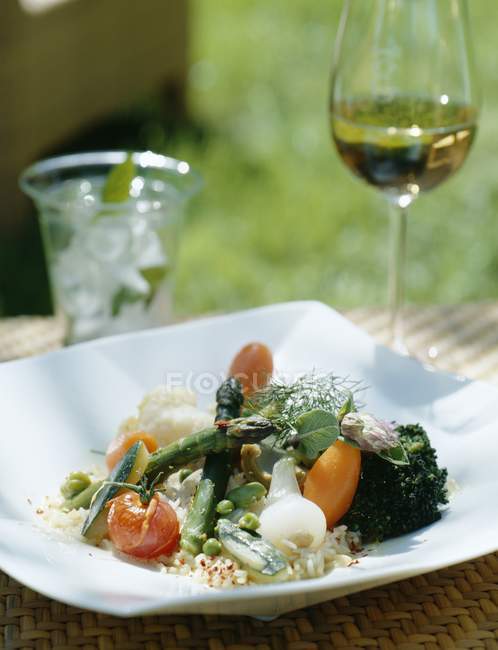 Insalata di verdure su piatto bianco sopra tavolo e vino in vetro su sfondo — Foto stock