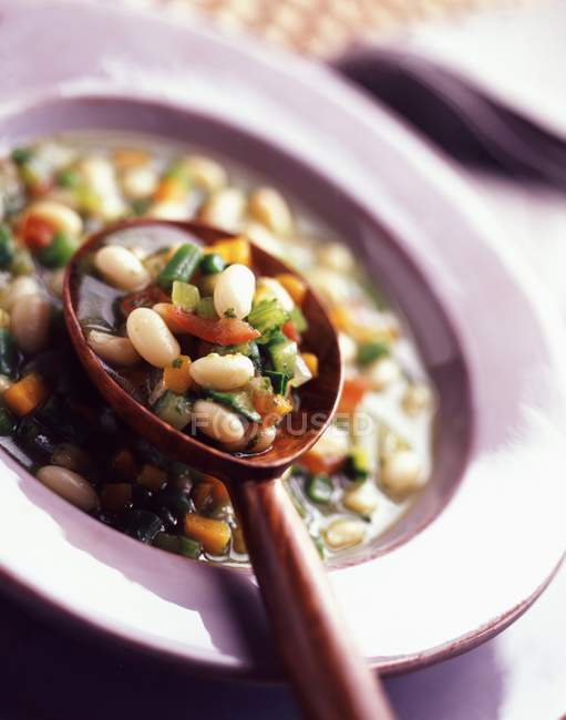 Zuppa di pistou aglio, basilico e verdure su piatto rosa con cucchiaio di legno — Foto stock