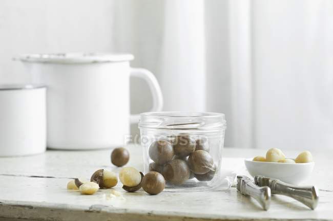 Vue rapprochée des noix de Macadamia dans un bocal en verre et un casse-noisette sur une table de cuisine rustique — Photo de stock