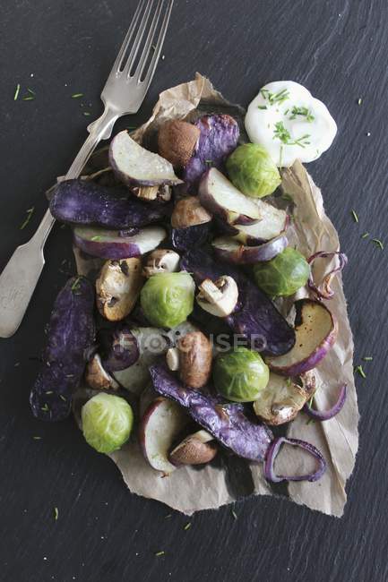 Oven-roasted winter vegetables with dill yoghurt dip on black wooden surface with fork — Stock Photo