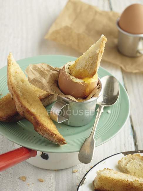 Крупный план варёного яйца и солдат на винтажной тарелке с серебряной ложкой — стоковое фото