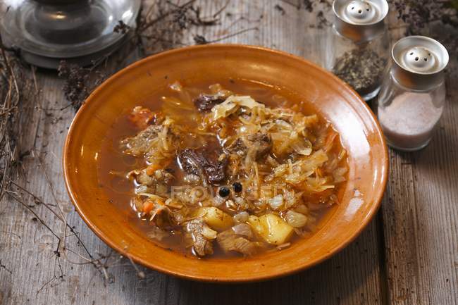 Cabbage soup on brown plate  over wooden surface — Stock Photo