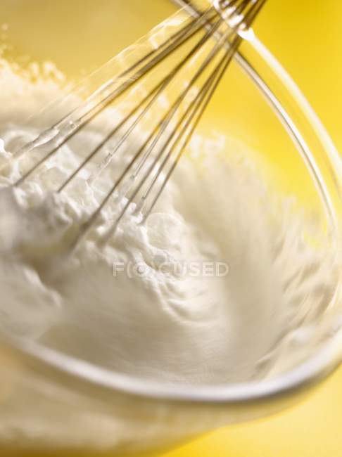 Whipping egg whites with a whisk in a glass bowl — Stock Photo