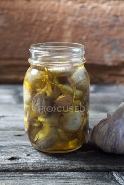 Preserved garlic in mason jar over wooden surface — Stock Photo