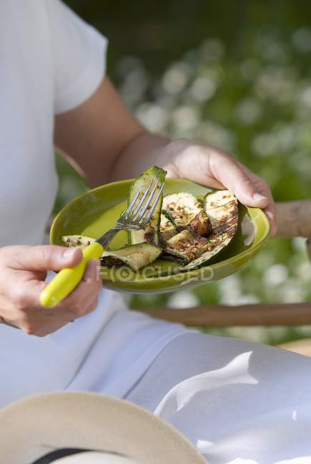 Pessoa comendo abobrinha grelhada ao ar livre na placa em mãos ao ar livre, midsection — Fotografia de Stock