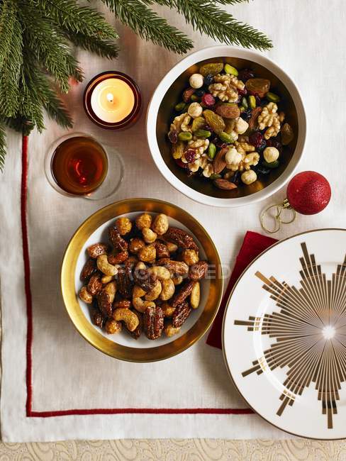 Top view of fruit and nut mixes in bowl by burning candle and Christmas bauble — Stock Photo