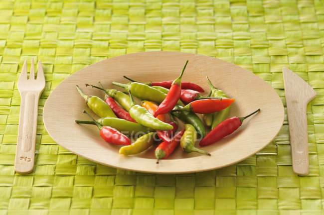 Wooden Plate of pimentos on green surface with fork and knife — Stock Photo