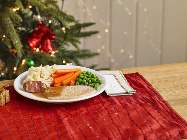Детская порция рождественского ужина с индейкой на белой тарелке над красным полотенцем — стоковое фото