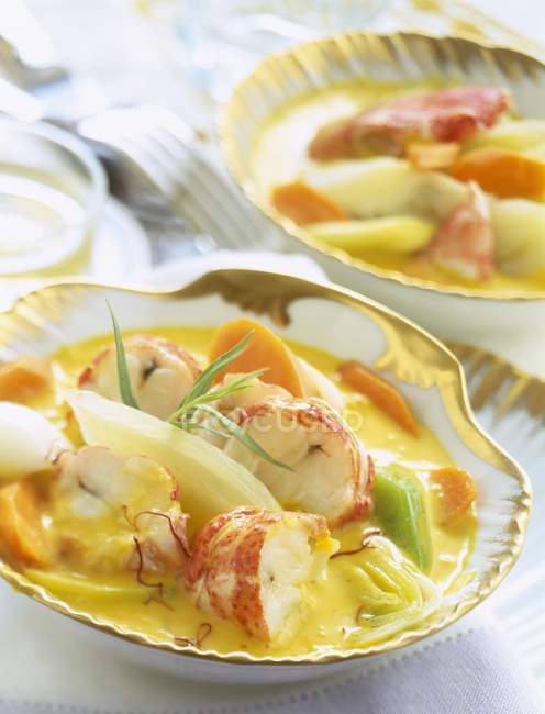 Lobster and vegetables in saffron-flavored stock on plates — Stock Photo