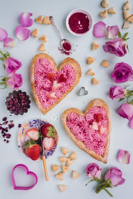Vista de cerca de las tartas de hojaldre en forma de corazón con crema de rosas, fresas y espolvoreos - foto de stock