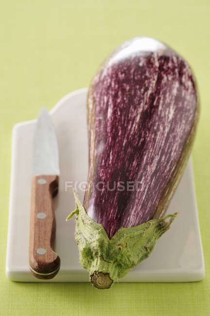 Purple eggplant on chopping board with knife — Stock Photo