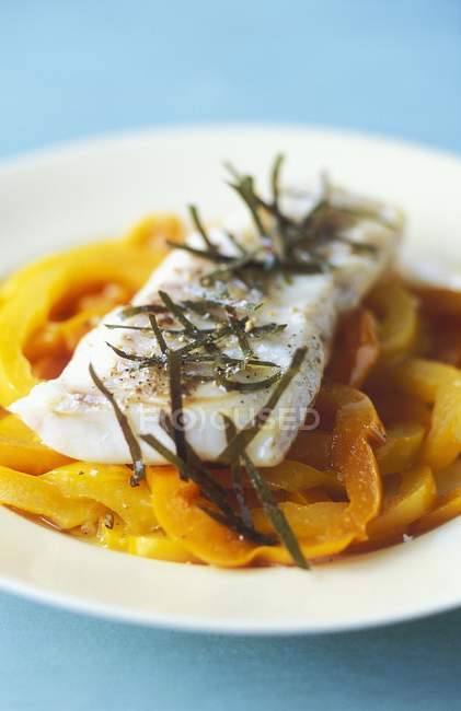 Cod fillet with bay leaves on a yellow pepper medley on white plate — Stock Photo