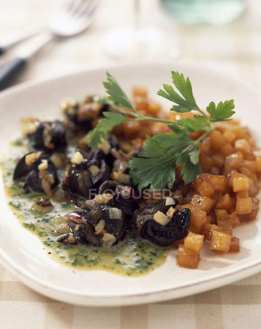 Snail fricase in parsley sauce with pan-fried Swedish turnips  on white plate — Stock Photo