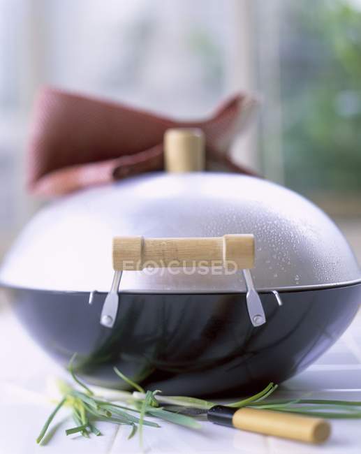 Vista close-up de wok fechado molhado com erva, faca e toalha — Fotografia de Stock