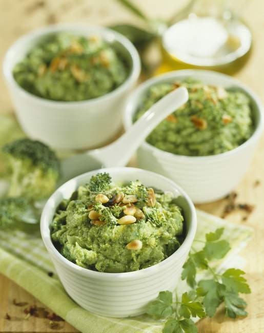 Individual broccoli purees with pine nuts in white pots — Stock Photo