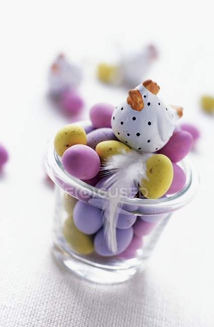 Closeup view of mini Easter eggs in glass with hen figurine and feather — Stock Photo
