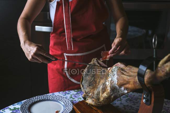 Vue recadrée de femme tranchant jambon Serrano — Photo de stock