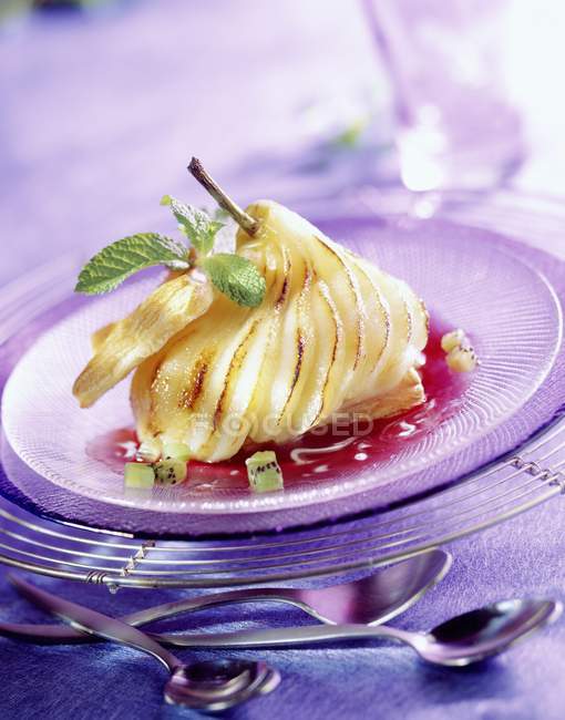 Closeup view of sliced roast pear with berry sauce, mint leaves and sliced kiwi on plate — Stock Photo