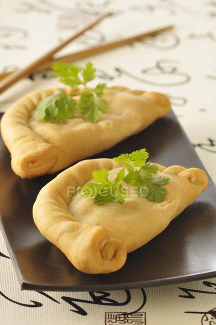 Chinese turnovers on small black plate — Stock Photo