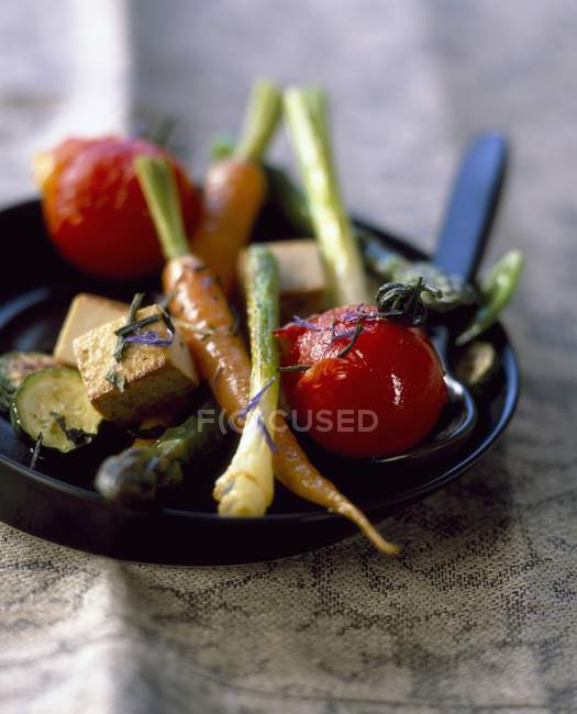 Fried vegetables with tofu and tea on black plate — Stock Photo