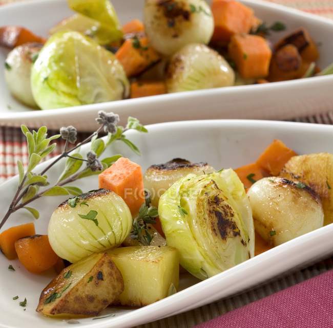 Cebollas a la parrilla, patatas y zanahorias en platos blancos - foto de stock