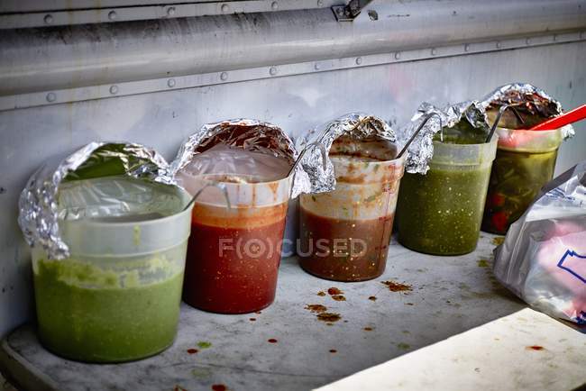Row of various sauces in plastic containers with foil caps and spoons — Stock Photo
