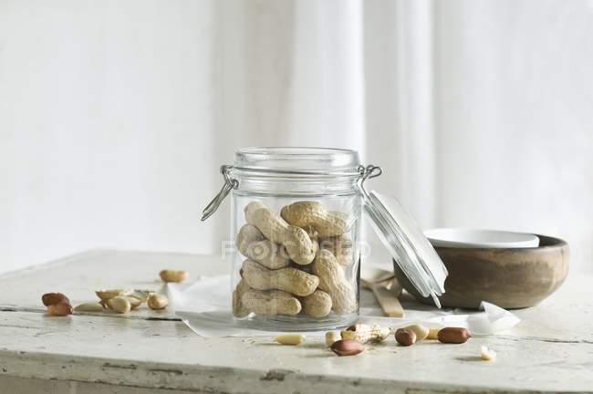 Peanuts in and next to a glass jar on a rustic kitchen table — Stock Photo