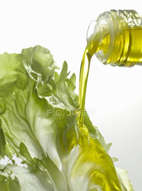 Aceite de oliva que cae sobre la hoja de lechuga - foto de stock
