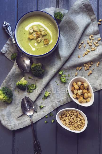 Creamy broccoli soup with pine kernels and croutons over towel — Stock Photo