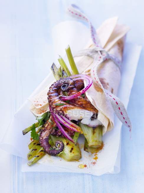 Small octopus and grilled fennel kebab on paper over blue surface — Stock Photo