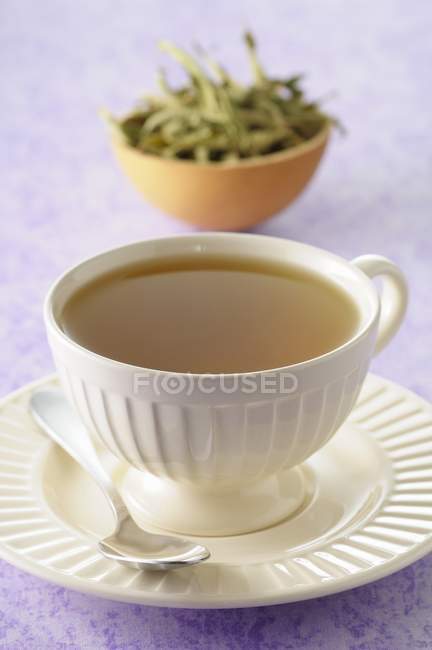 Cup of verbana over small plate on purple surface — Stock Photo