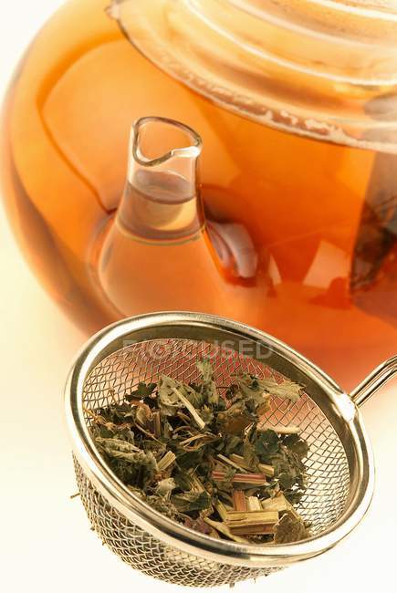Vue rapprochée des feuilles de thé sèches dans le tamis et la théière — Photo de stock