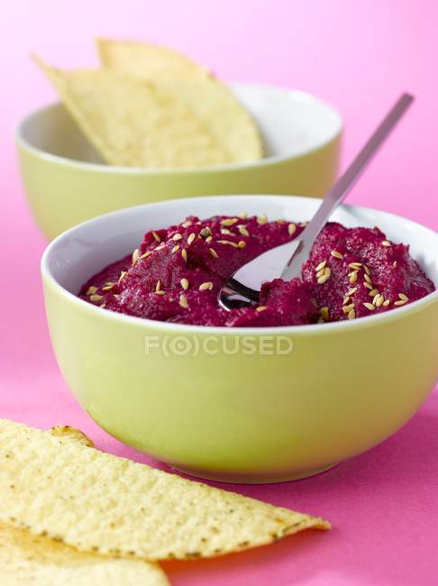 Hummus di barbabietola in ciotola gialla con cucchiaio sulla superficie rosa — Foto stock