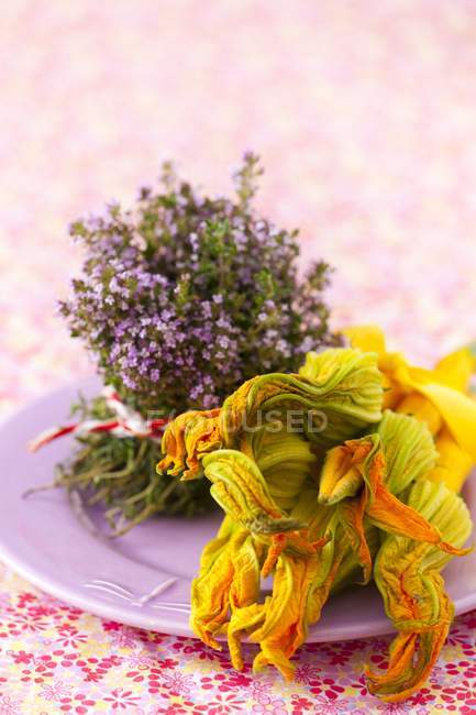 An arrangement of blossoming thyme and yellow courgette with flowers on a plate — Stock Photo