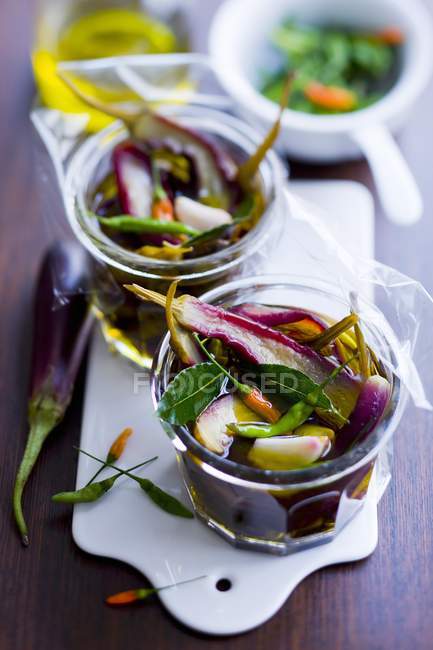 Pickled eggplants and bird peppers in glass jars over desk — Stock Photo