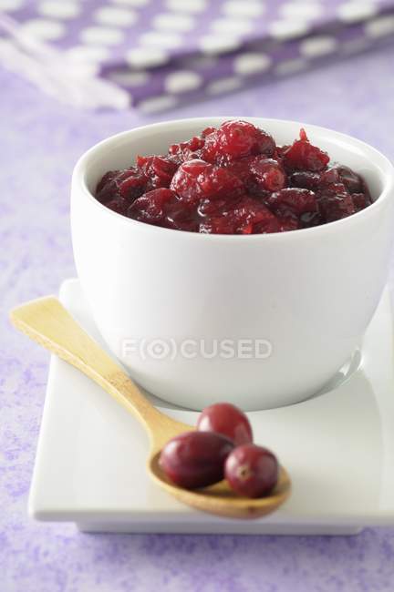 Stewed cranberries in white pots over plate with wooden spoon — Stock Photo
